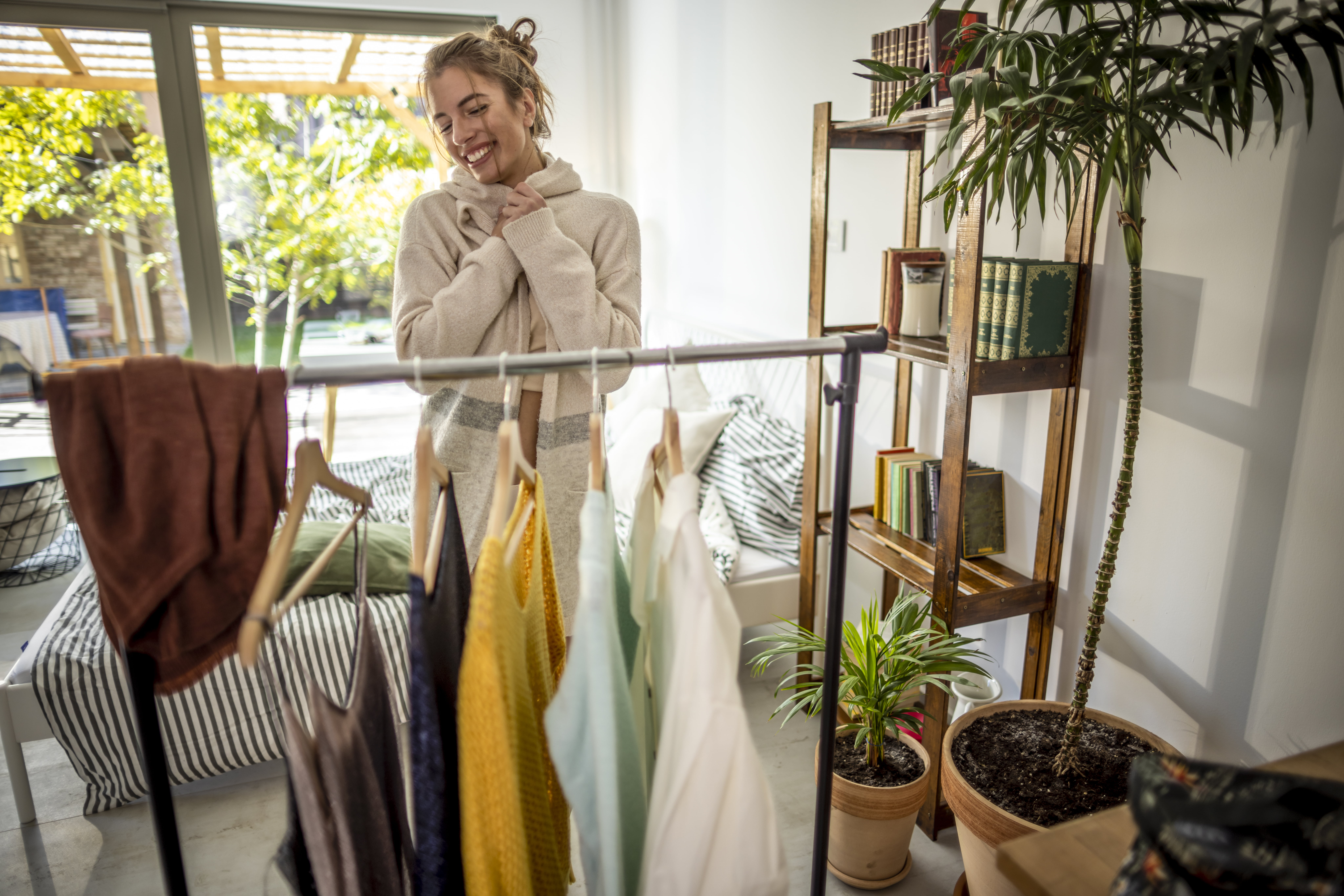 Kvinne står i garderoben og smiler medan ho held ein genser. Ho ryddar blant kleda sine i eit lyst og roleg rom.