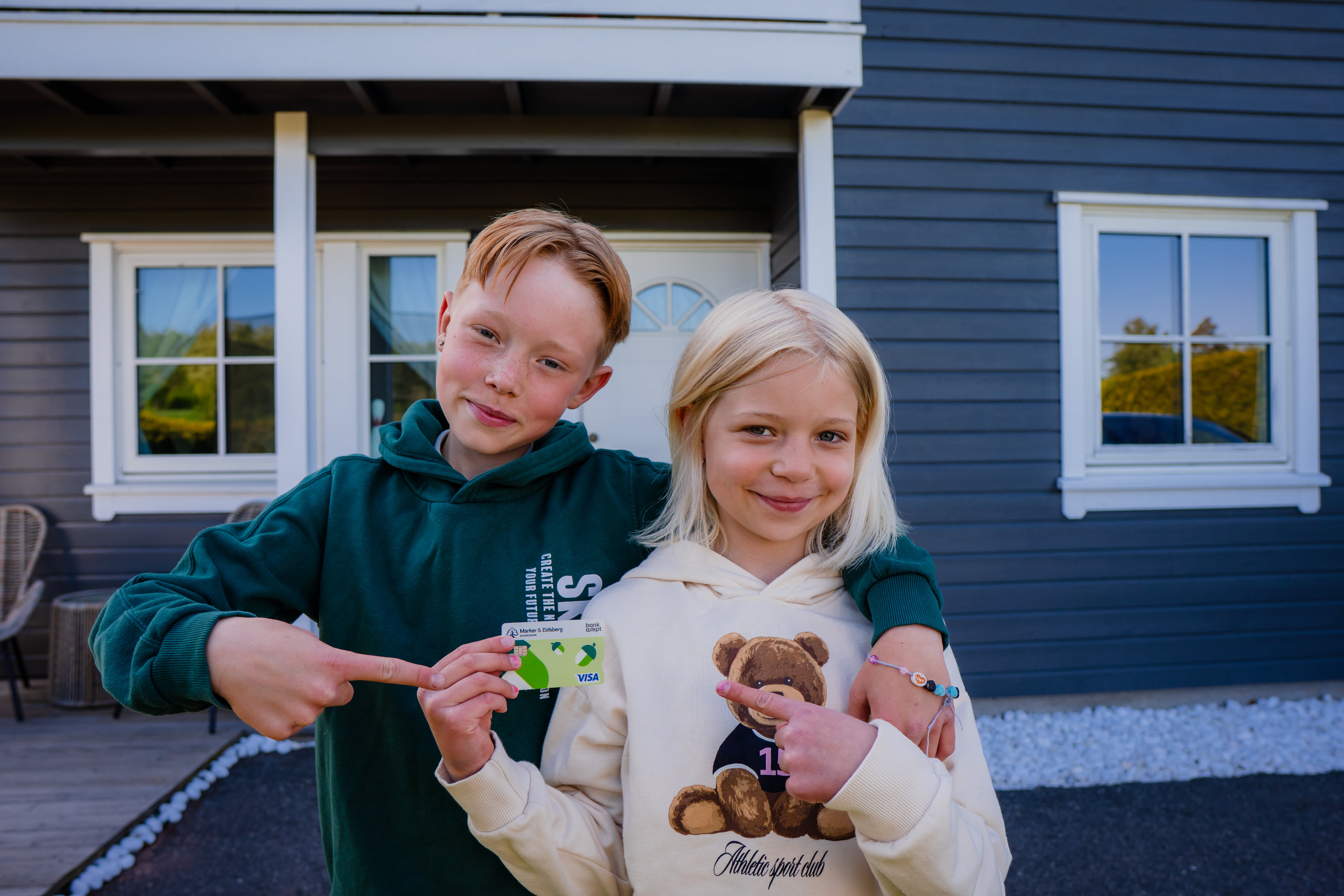 En liten gutt og en liten jente viser frem et bankkort.