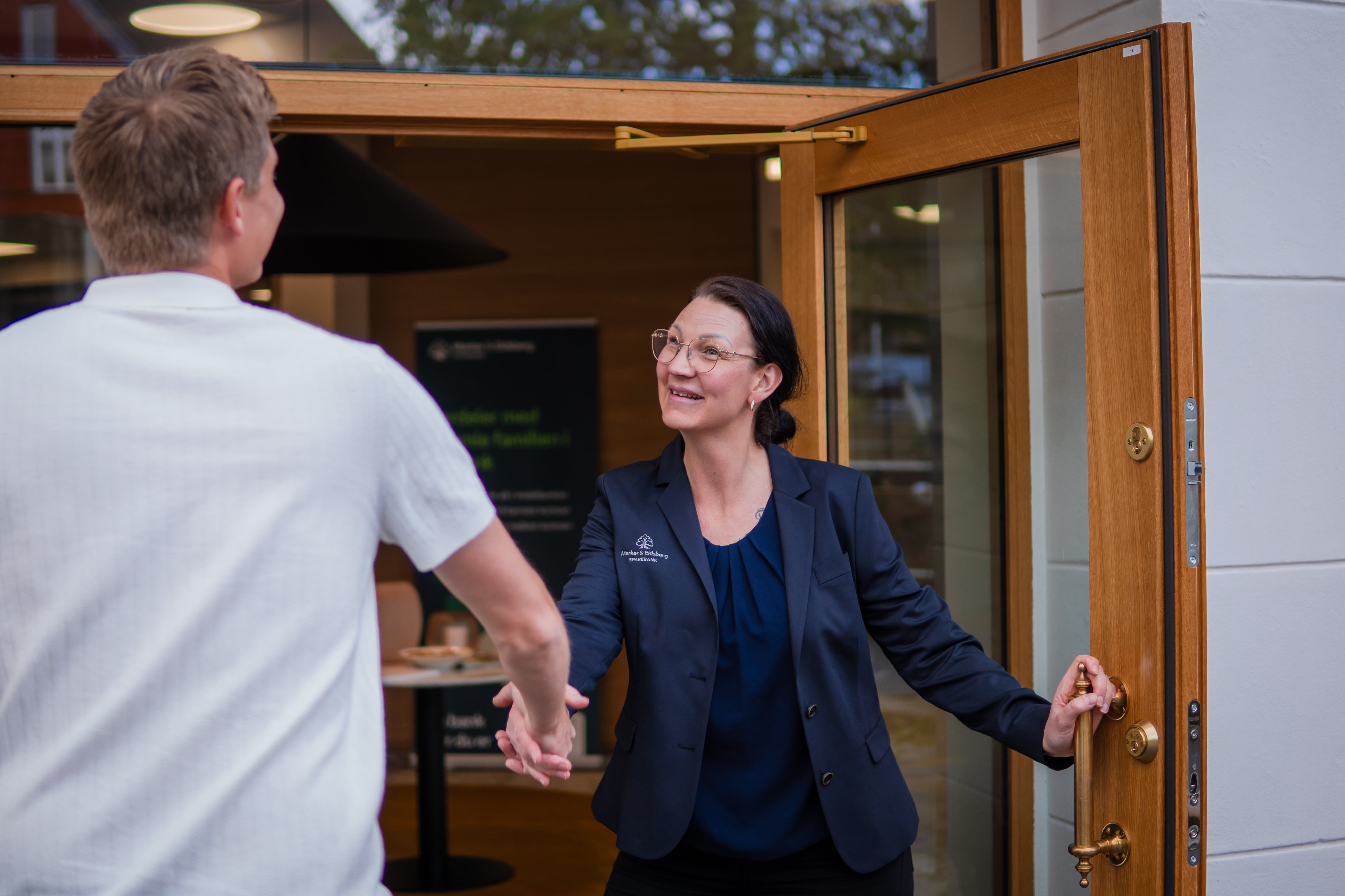 En kvinne iført dress tar imot en mann med lys t-skjorte med et håndtrykk utenfor et lokalkontor.