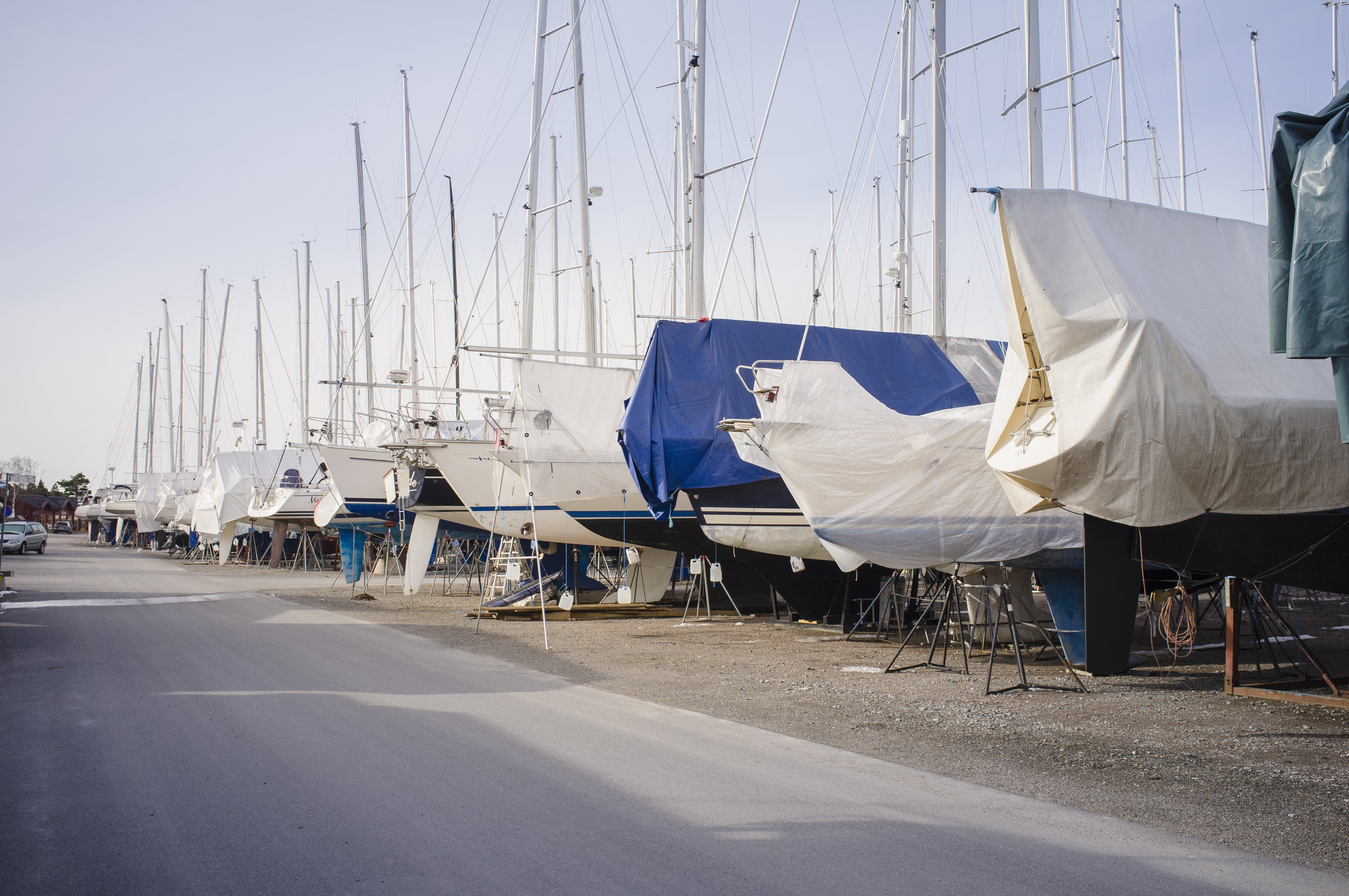 Seilbåter på land dekket med presenninger for vinteropplag, linet opp i en marina med master som stikker opp i bakgrunnen mot en klar himmel